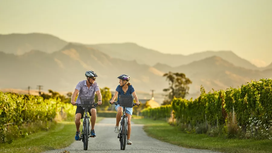 Couple cycling along vineyard road with mountain views in Marlborough wine region