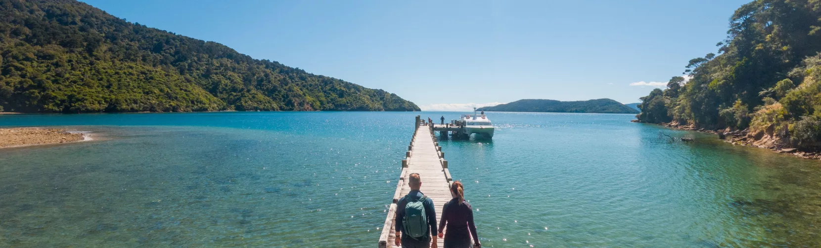Couple walking along the jetty at Ship Cove on the Queen Charlotte Track