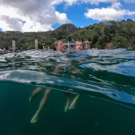 Couple floating in front of Punga Cove Resort with lush greenery behind.