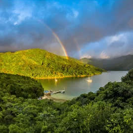 Double rainbow stretching over the lush bay and hills near Punga Cove Resort.
