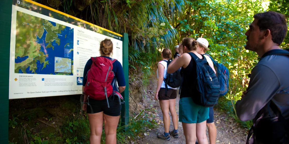 Group of hikers reading a trail map at Ship Cove on the Queen Charlotte Track in Marlborough.