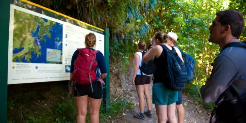 Group of hikers reading a trail map at Ship Cove on the Queen Charlotte Track in Marlborough.