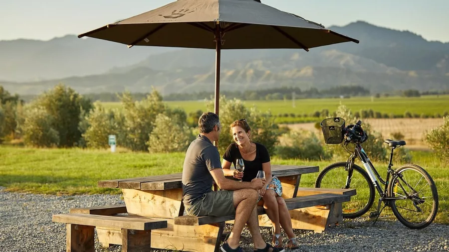 Couple enjoying wine at a shaded vineyard rest stop during a Marlborough cycling tour