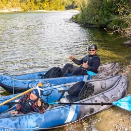 Two kayakers giving thumbs up while seated in inflatable rafts on the riverbank