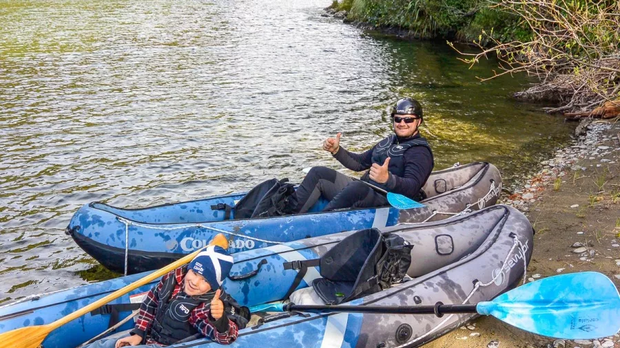 Two kayakers giving thumbs up while seated in inflatable rafts on the riverbank