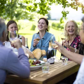 Group laughing and toasting wine over an alfresco lunch in a vineyard
