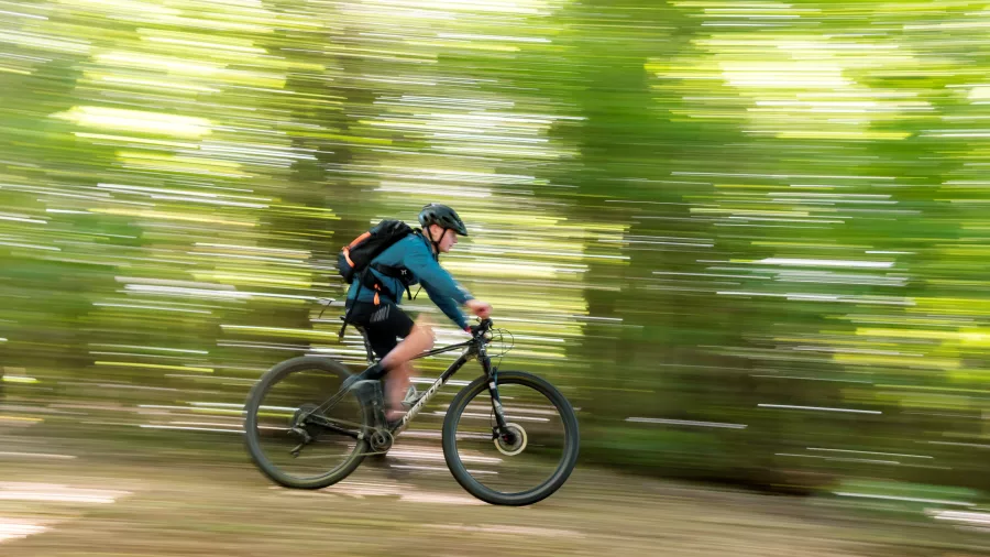 Cyclist with backpack riding quickly through the forest on the Queen Charlotte Track.