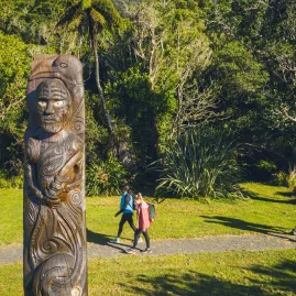 Walkers passing a Māori carving at Ship Cove on the Queen Charlotte Track