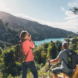 Couple capturing the coastal scenery from a lookout bench on the Queen Charlotte Track near Ship Cove