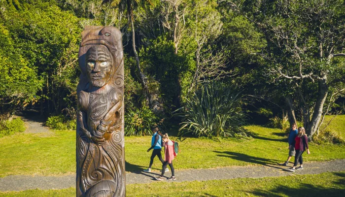 Walkers passing a Māori carving at Ship Cove on the Queen Charlotte Track
