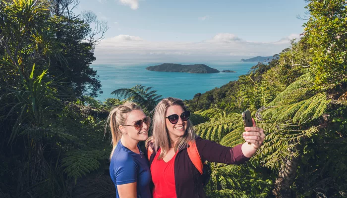 Two women take a selfie with scenic ocean views behind them on Queen Charlotte Track