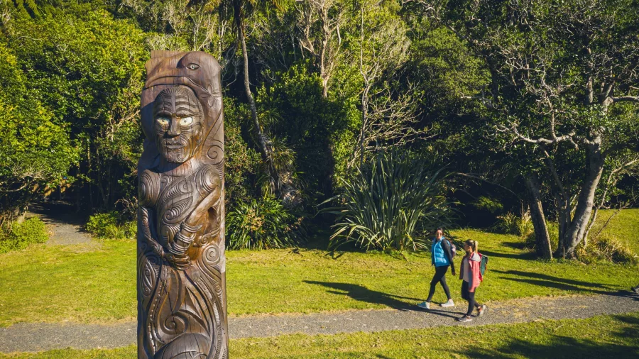 Hikers walking near a carved Māori totem at Ship Cove in Marlborough