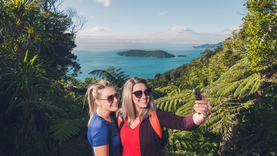 Two women take a selfie with scenic ocean views behind them on Queen Charlotte Track