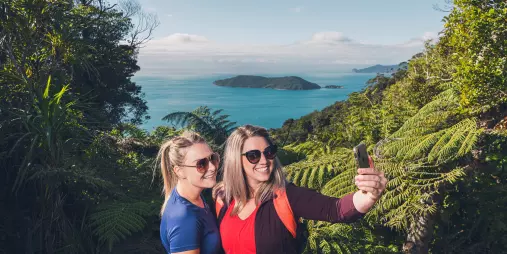 Two women take a selfie with scenic ocean views behind them on Queen Charlotte Track