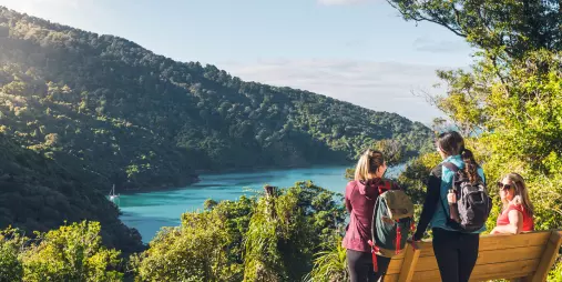 Family resting at a scenic viewpoint overlooking the water near Ship Cove on the Queen Charlotte Track