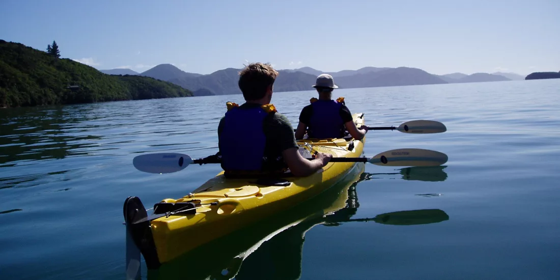Two people kayaking on calm waters in Queen Charlotte Sound, Marlborough