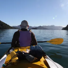 Solo kayaker paddling through calm morning waters in Queen Charlotte Sound
