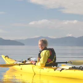 Kayaker smiling in a yellow kayak on a guided tour in Marlborough’s Queen Charlotte Sound