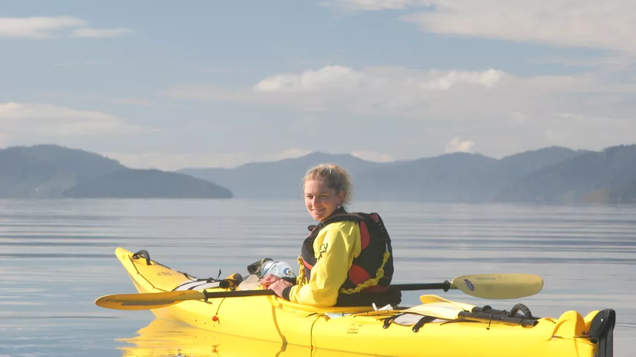 Kayaker smiling in a yellow kayak on a guided tour in Marlborough’s Queen Charlotte Sound