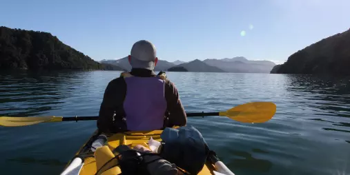 Solo kayaker paddling through calm morning waters in Queen Charlotte Sound