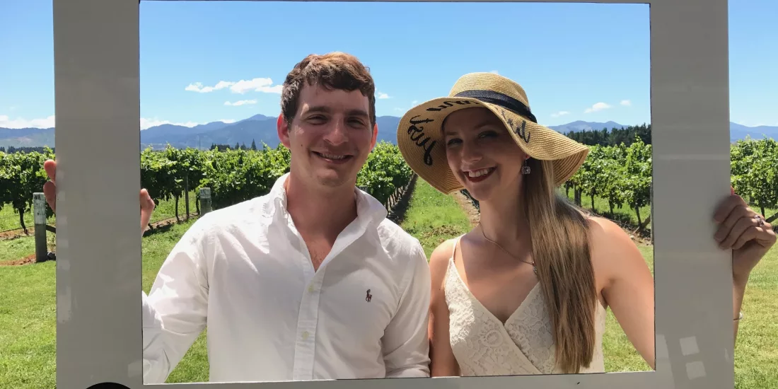 Couple posing with a Spy Valley Wines photo frame in front of vineyard rows.