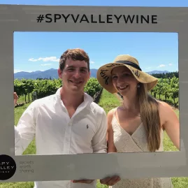Couple posing with a Spy Valley Wines photo frame in front of vineyard rows.