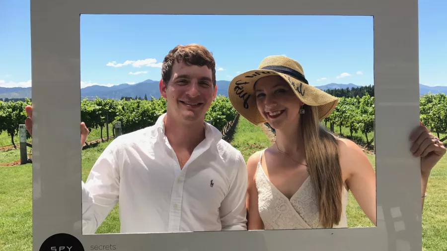 Couple posing with a Spy Valley Wines photo frame in front of vineyard rows.