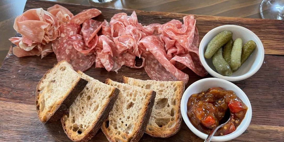Wooden board with artisan bread, salami, cornichons, and chutney at Cloudy Bay Winery.