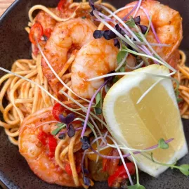 Bowl of prawn linguine pasta with lemon wedge and microgreens