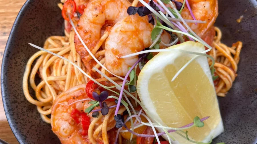 Bowl of prawn linguine pasta with lemon wedge and microgreens