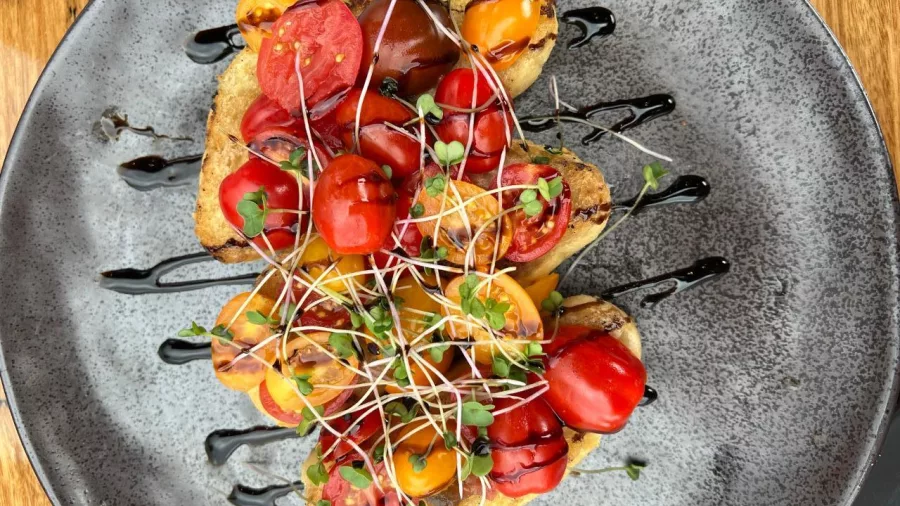 Colourful heirloom tomato bruschetta topped with balsamic glaze and microgreens