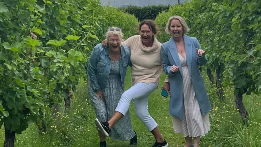 Group of women laughing and posing in a lush green vineyard