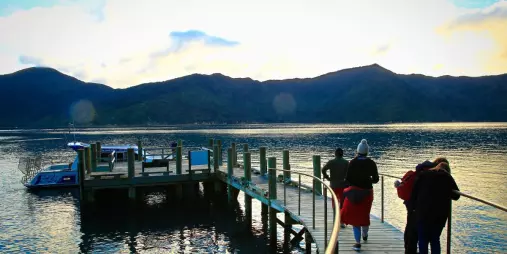 Tour group walking along Ship Cove jetty in the Marlborough Sounds at sunrise