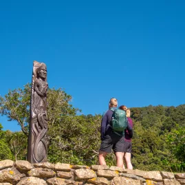 Travellers admiring a tall Pouwhenua (Maori carving) on Queen Charlotte Track at Ship Cove