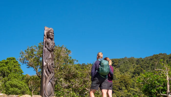 Travellers admiring a tall Pouwhenua (Maori carving) on Queen Charlotte Track at Ship Cove