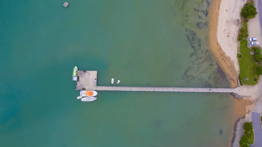 Drone shot of Ship Cove jetty stretching into the blue-green waters of Queen Charlotte Sound