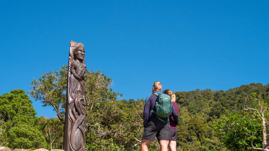 Travellers admiring a tall Pouwhenua (Maori carving) on Queen Charlotte Track at Ship Cove