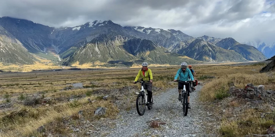 Two cyclists riding a gravel trail through the Southern Alps near Mount Cook, New Zealand
