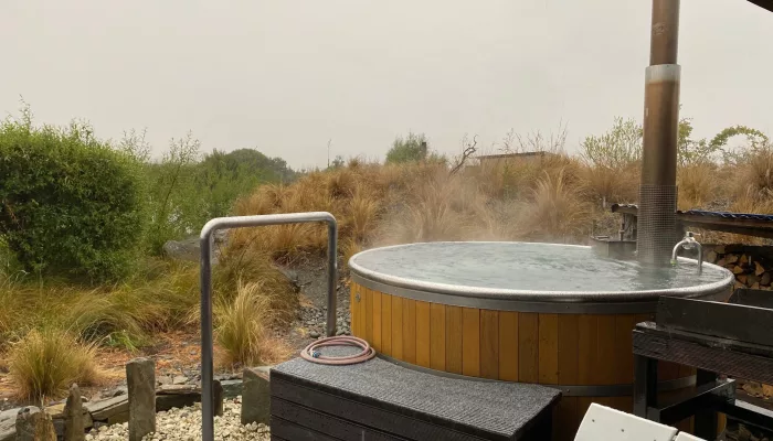Steaming outdoor hot tub at Omarama surrounded by native plants on a misty day