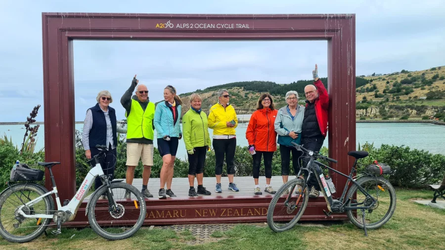 Group of cyclists celebrating at the Alps 2 Ocean Cycle Trail finish line in Oamaru, New Zealand.