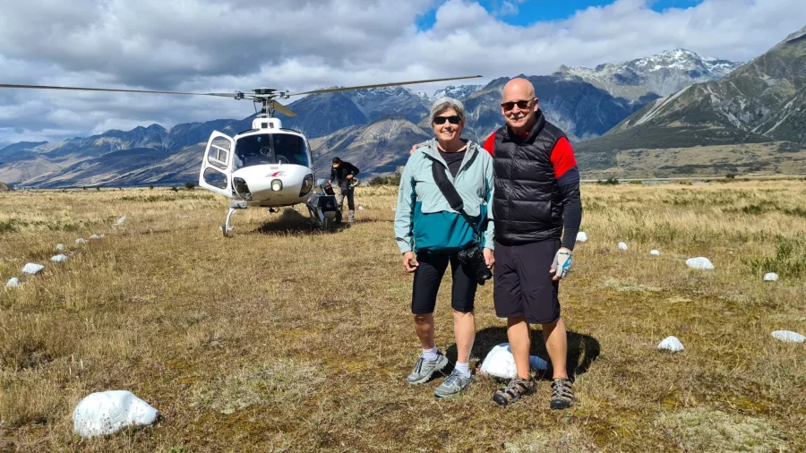 Couple standing near a helicopter with the Tasman River valley and Southern Alps in the background.