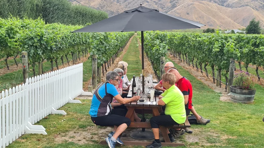 Group enjoying wine tasting and lunch at a vineyard table under an umbrella at Kurow Winery