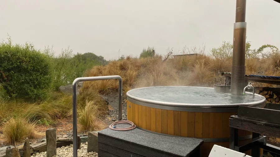 Steaming outdoor hot tub at Omarama surrounded by native plants on a misty day