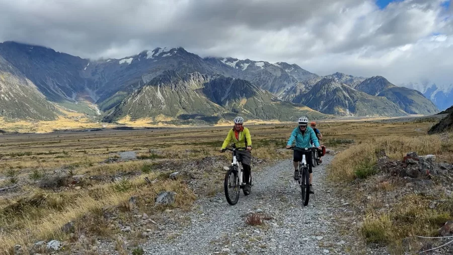 Two cyclists riding a gravel trail through the Southern Alps near Mount Cook, New Zealand
