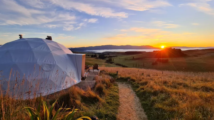 Sunset over a scenic valley with a glamping dome in New Zealand