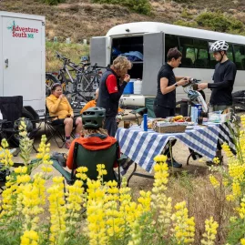 Cyclists enjoying a catered meal stop beside the Adventure South NZ support vehicle during a guided tour.