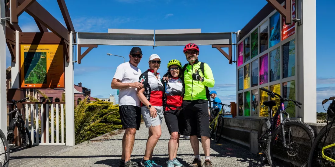Group of cyclists posing at the Greymouth start point of the West Coast Wilderness Trail in New Zealand.