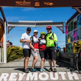 Group of cyclists posing at the Greymouth start point of the West Coast Wilderness Trail in New Zealand.