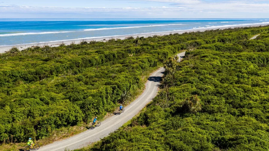 Cyclists riding along a scenic coastal trail on New Zealand's West Coast Wilderness Trail with ocean views.