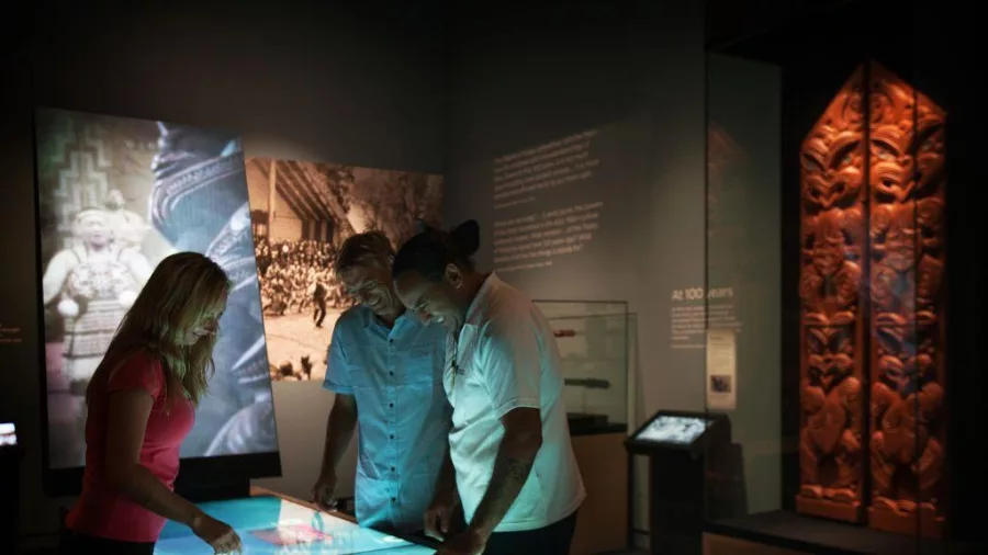 Visitors interacting with an illuminated touchscreen exhibit at the Waitangi Treaty Grounds Museum in Paihia